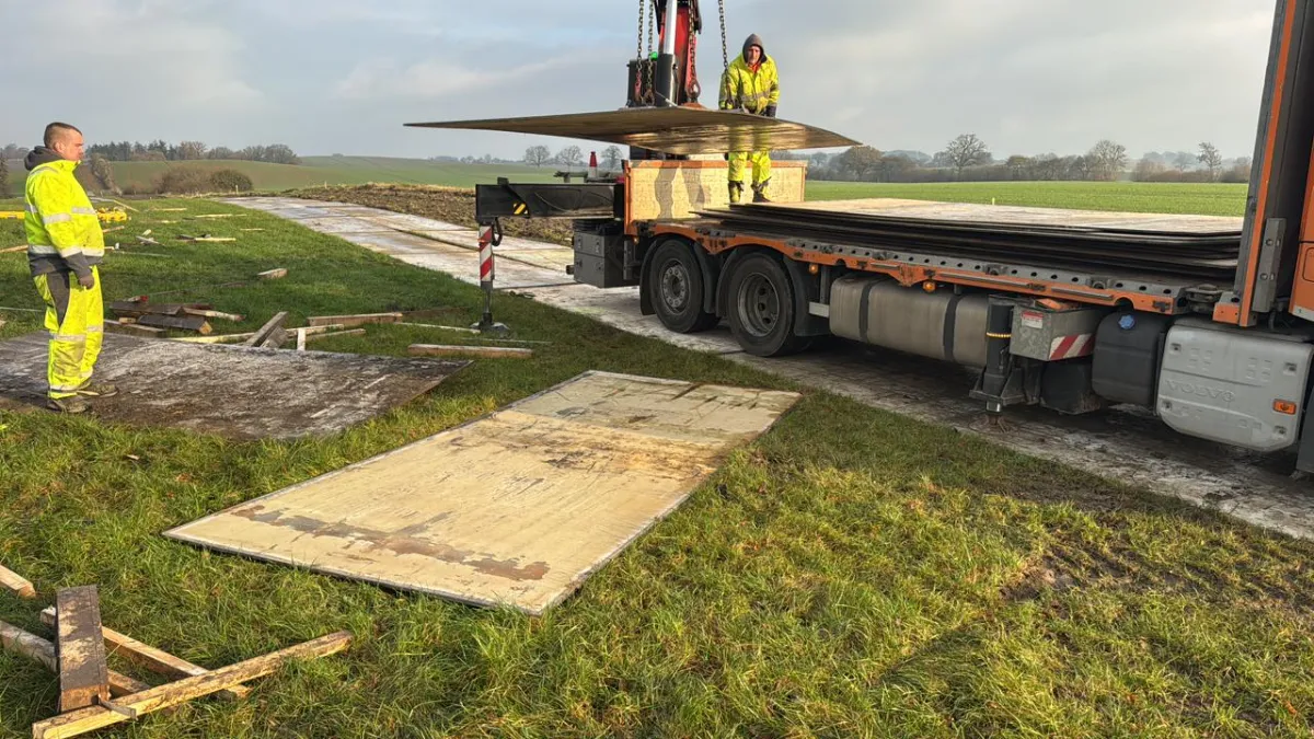 Kranverladung von Überfahrplatten aus Stahl auf Baustelle im Grünen